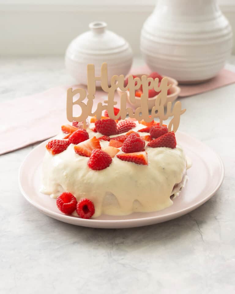 Smash Cake served on a blush pink plate, topped with frosting and garnished with halved strawberries, raspberries and topped with "Happy birthday" sign.