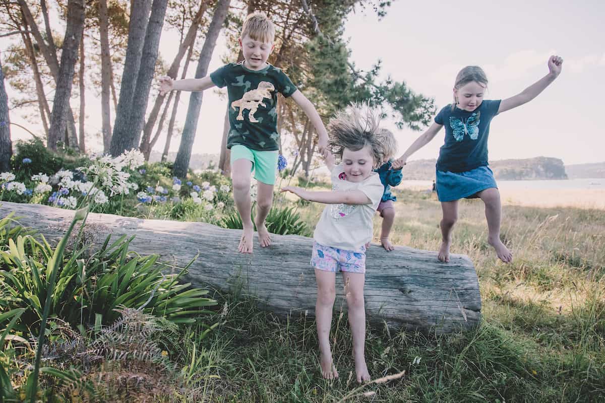 4 happy children jumping off a log