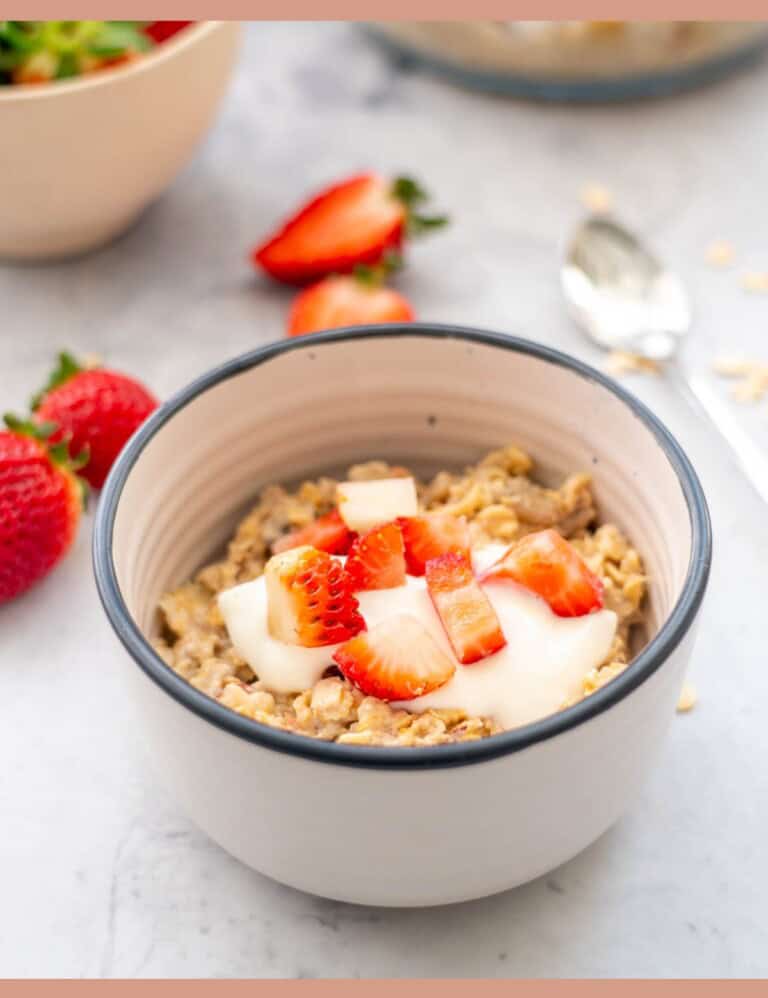 A bowl of muesli topped with yogurt and chopped strawberries.
