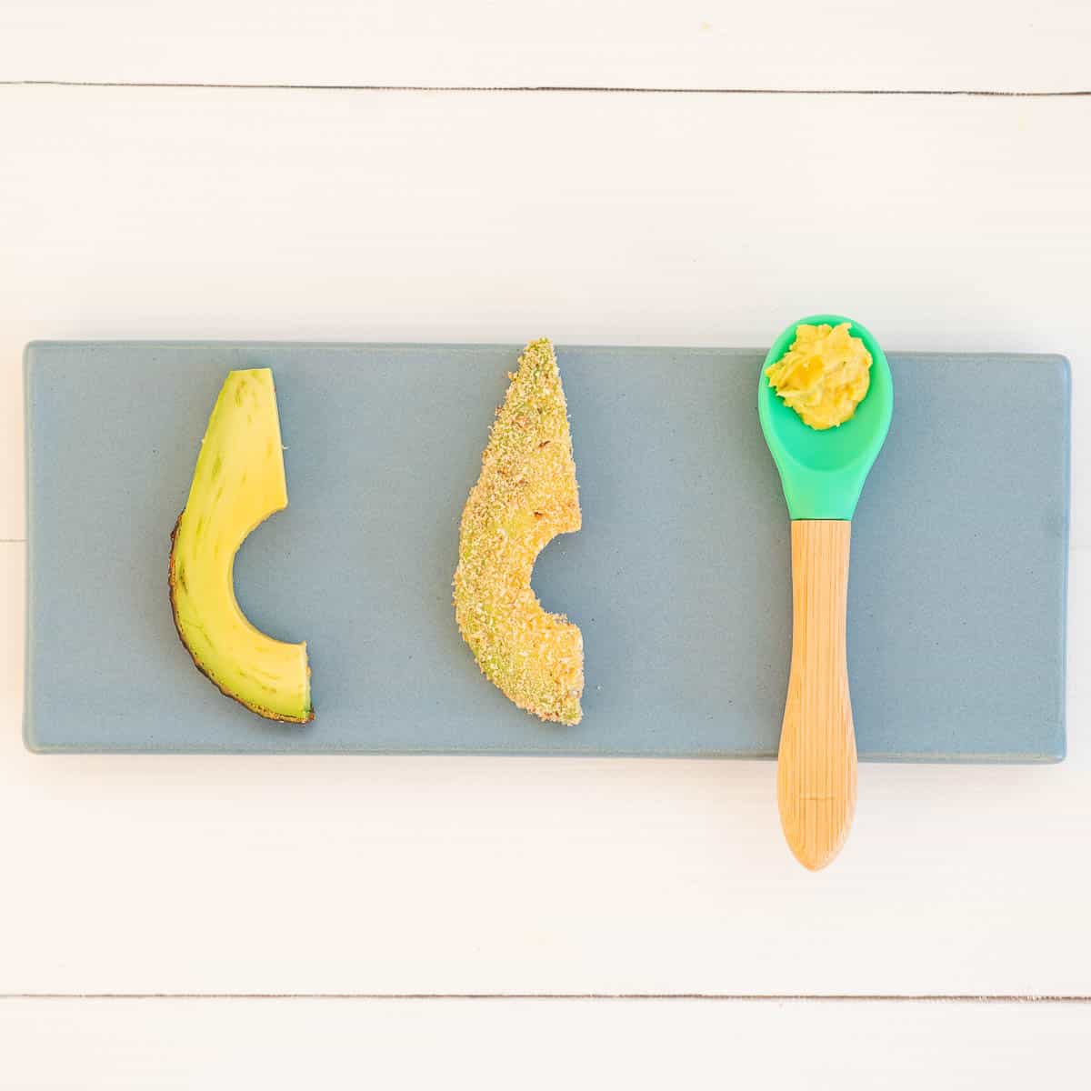 Avocado slice with half skin in place, crumbed avocado slice and avocado baby food pre-loaded on a green silicone baby spoon