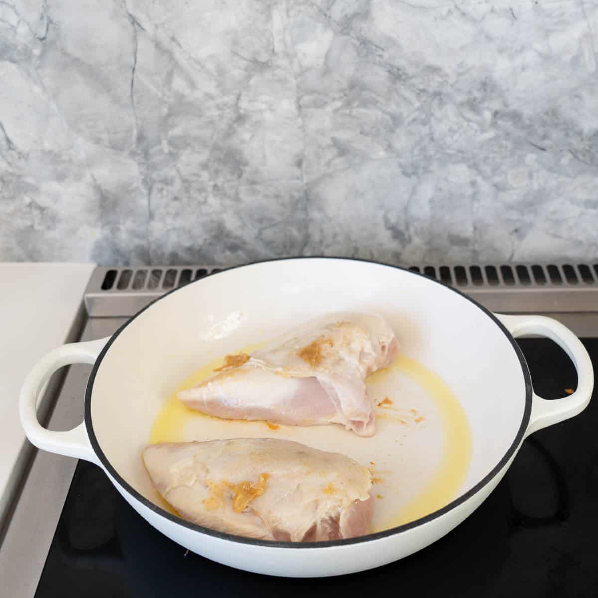 Two chicken breasts with golden cooked skin in a large white casserole dish. 