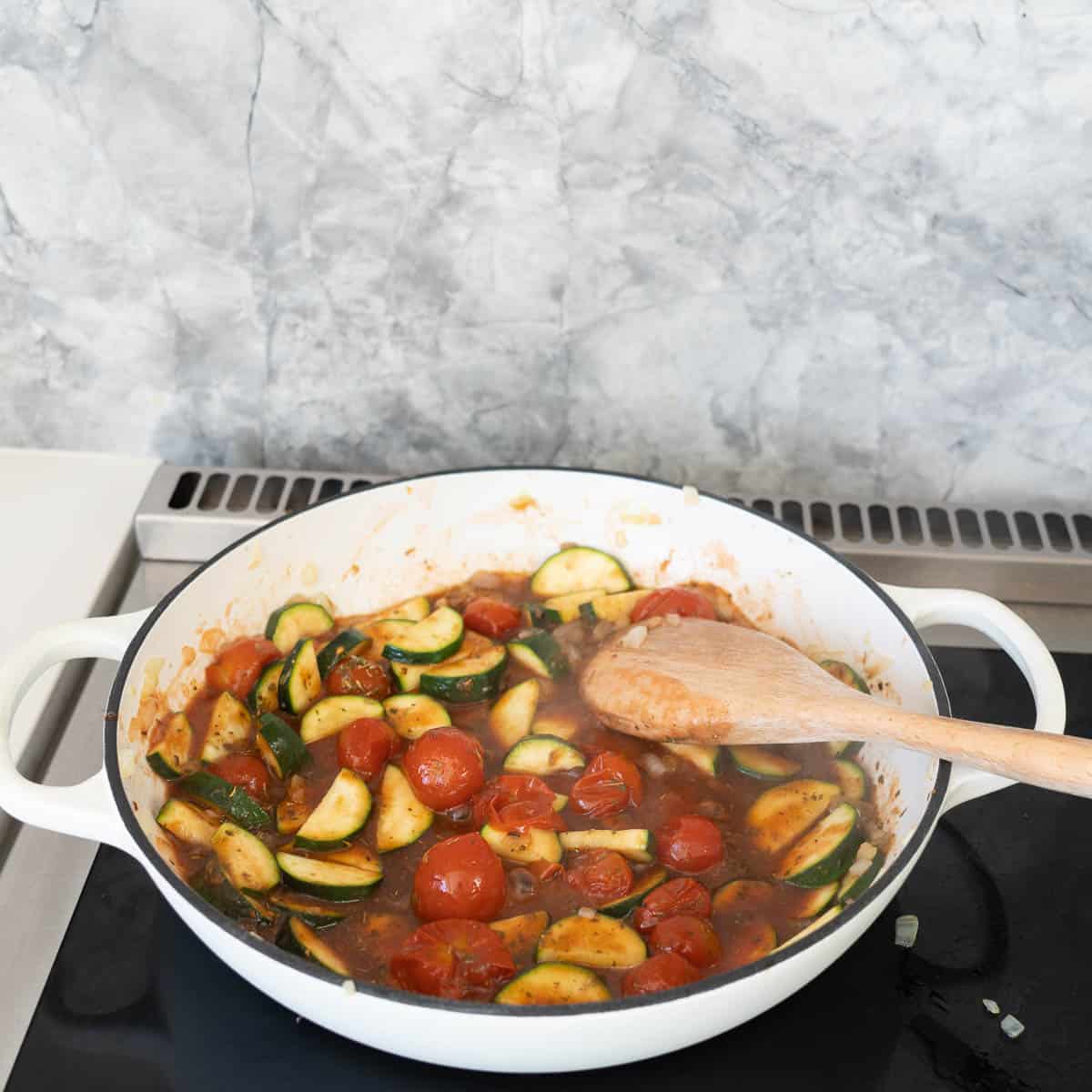 A tomato and vegetable sauce simmering in a white casserole dish.