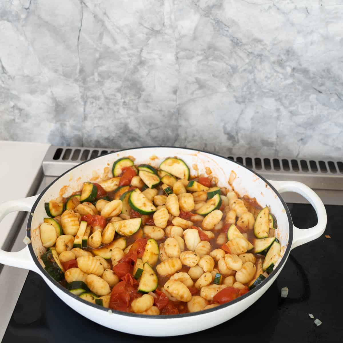 Gnocchi in a tomato and vegetable sauce in a large white casserole dish.