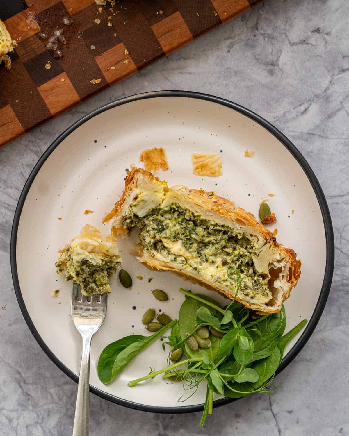 A slice of spinach pie on a plate with a side salad. 