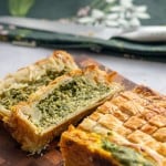 Two slices of pie on a wooden chopping board showing the green spinach and cheese filling.