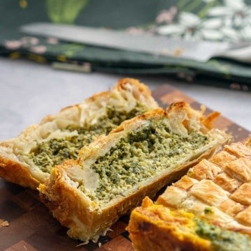 Two slices of pie on a wooden chopping board showing the green spinach and cheese filling.