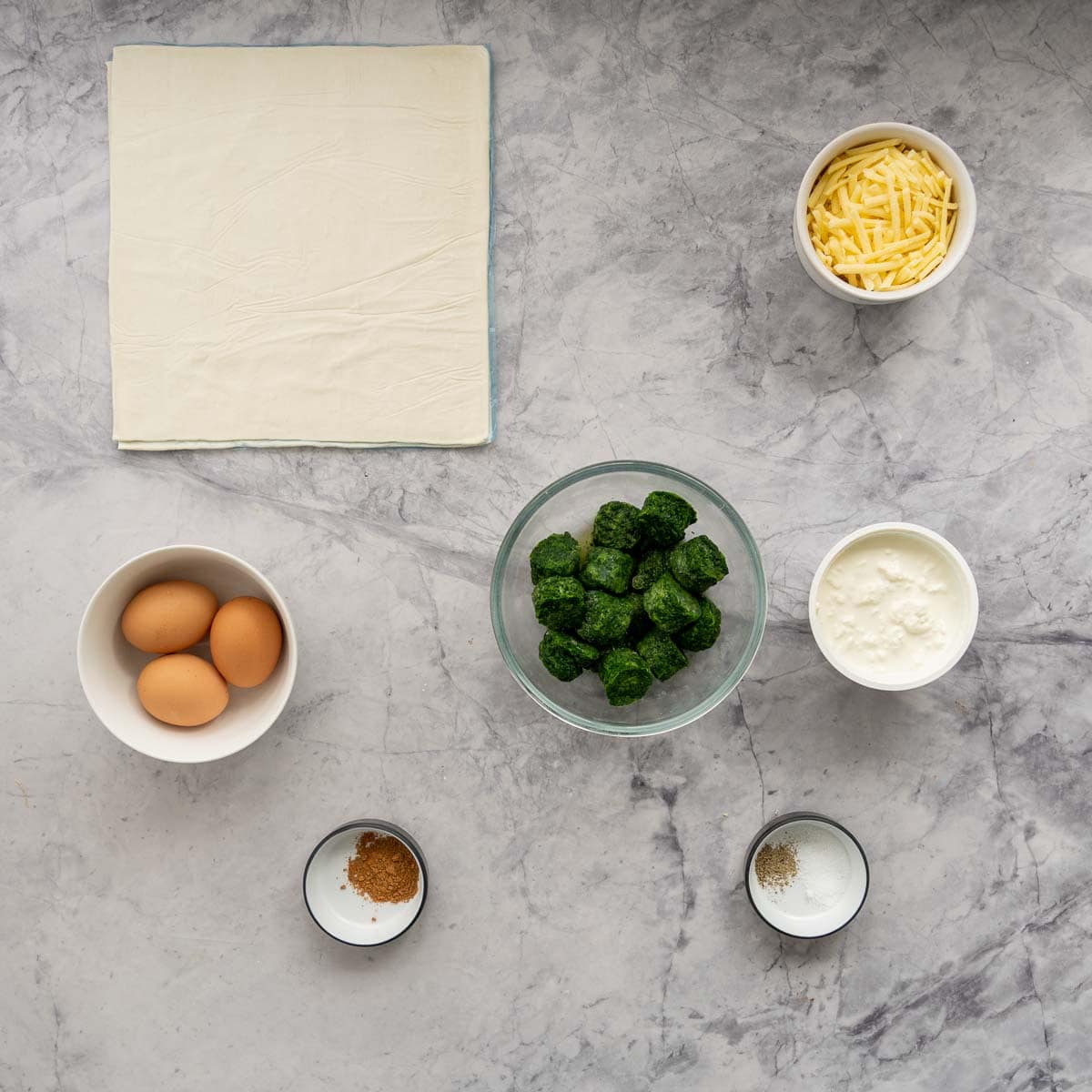 The ingredients to make spinach pie laid out on a marble bench top.