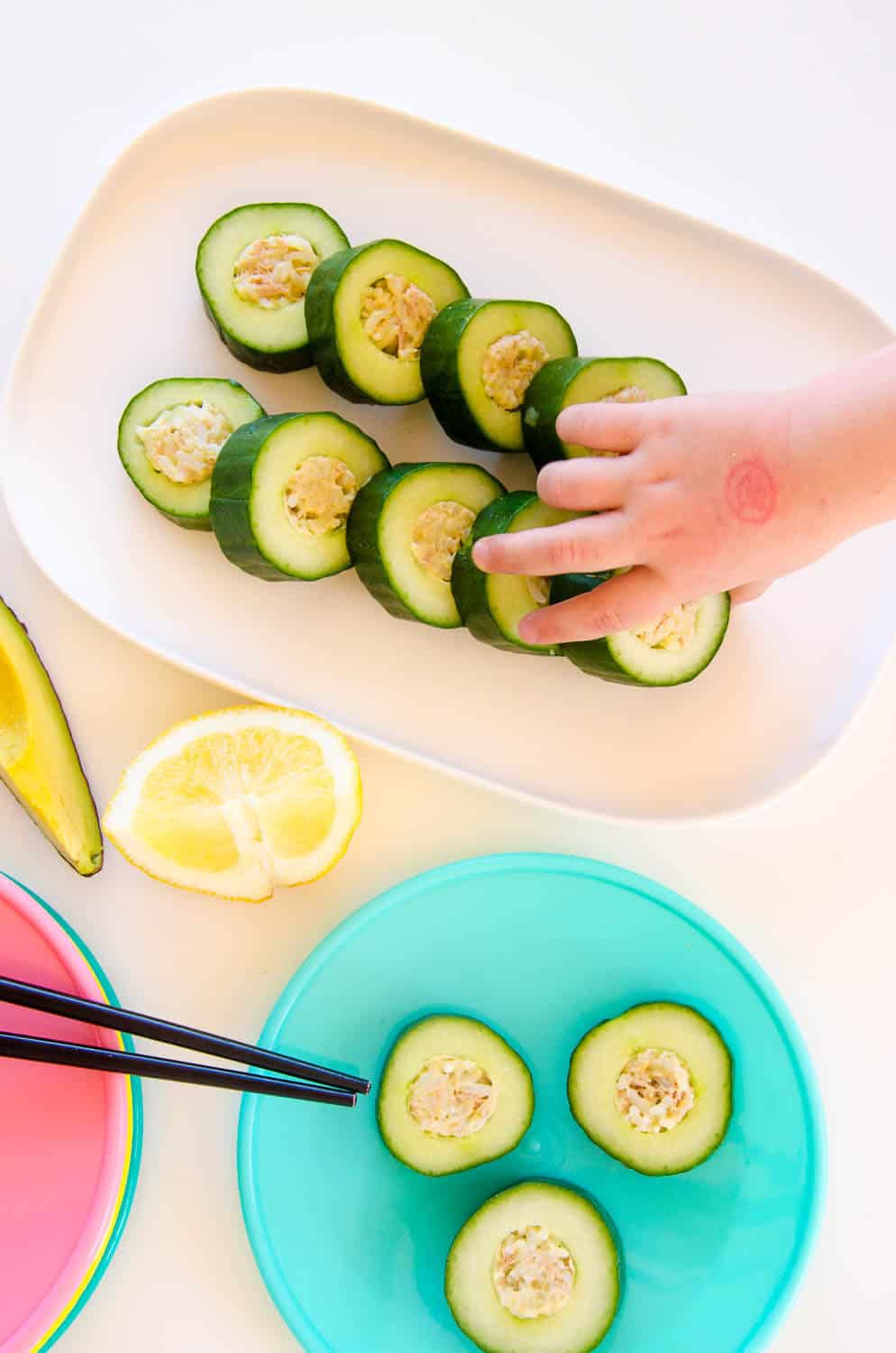 Table laid out with a sushi platter and colourful plates, child hand reaching for a piece of sushi