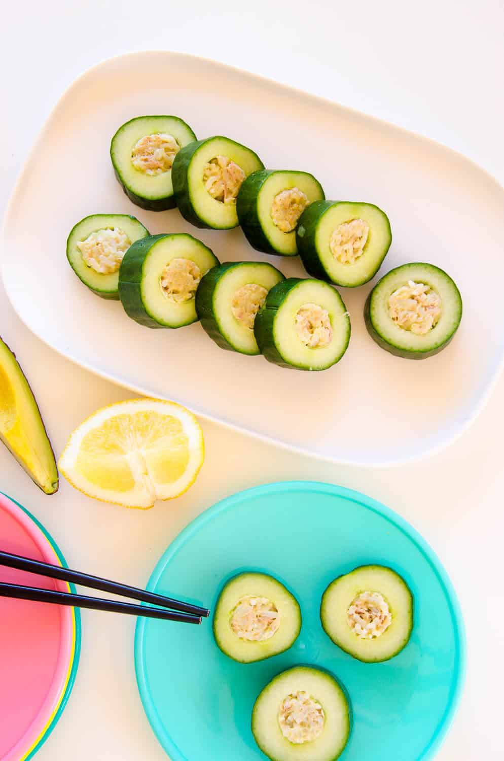 Table laid out with a platter of cucumber sushi, lemon slices, avocado and colourful plates