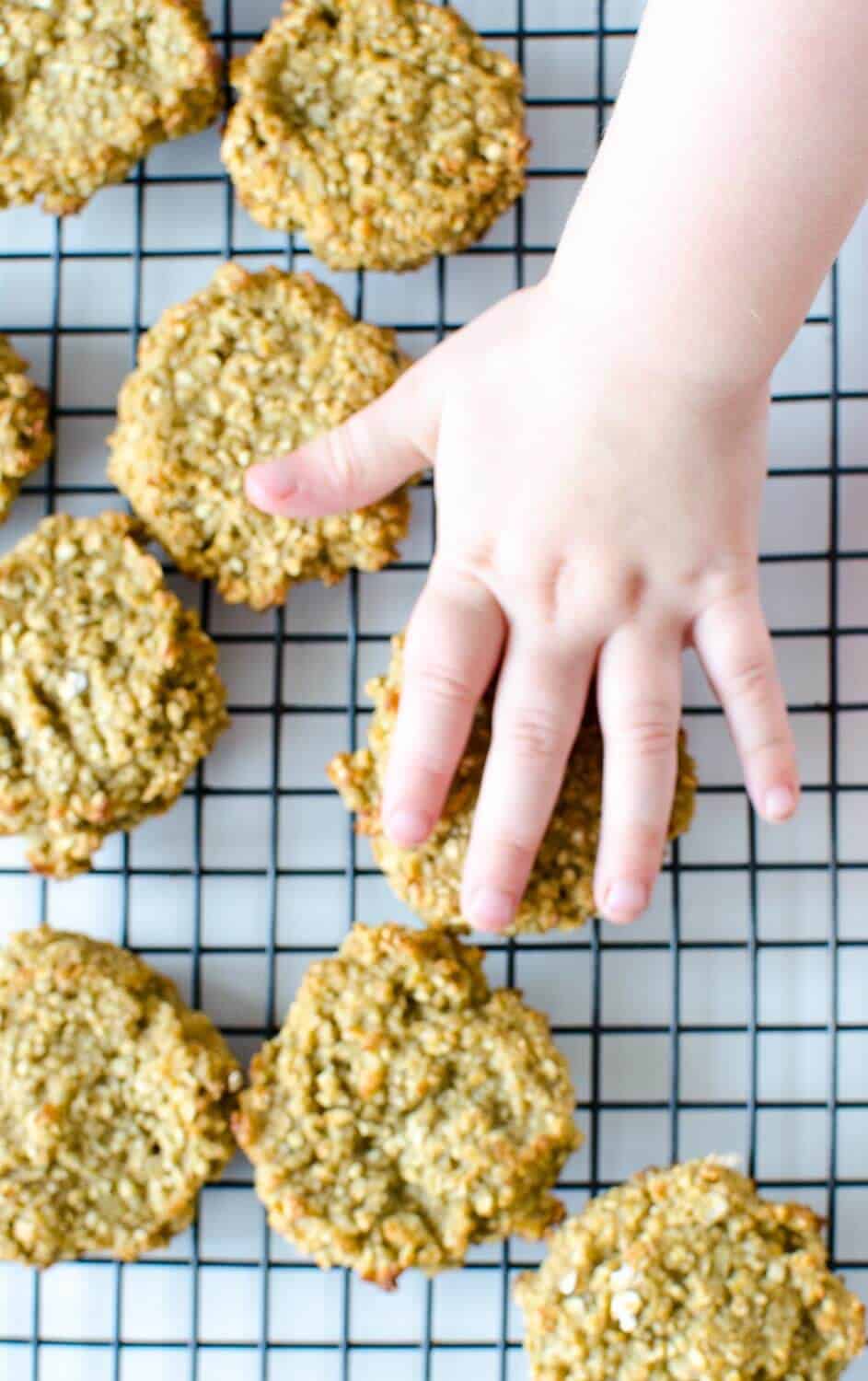 A childs hand reaching for oatmeal cookies cooling on a wire rack.