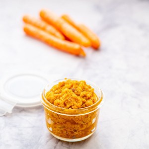 A small glass jar of orange pesto with loose baby carrots in the background.