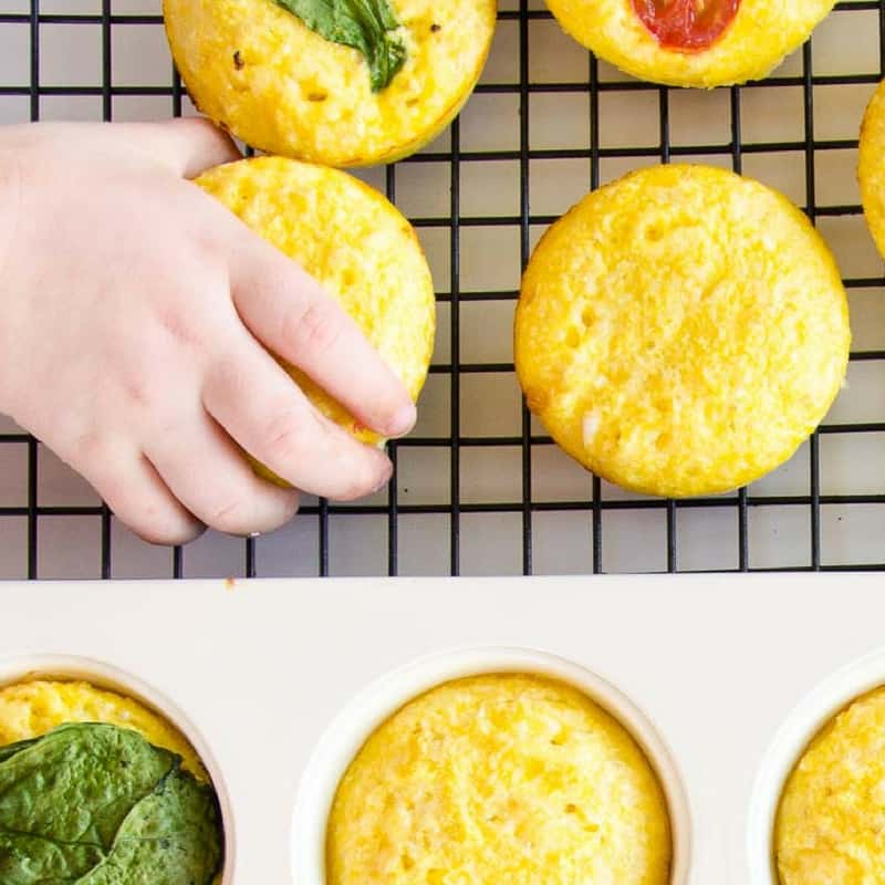 A child's hand reaching for an egg muffin cooling on a cooling rack.