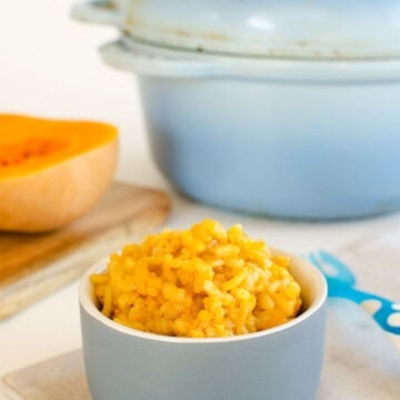 A ramekin of pumpkin risotto infant of a blue ceramic Dutch oven.