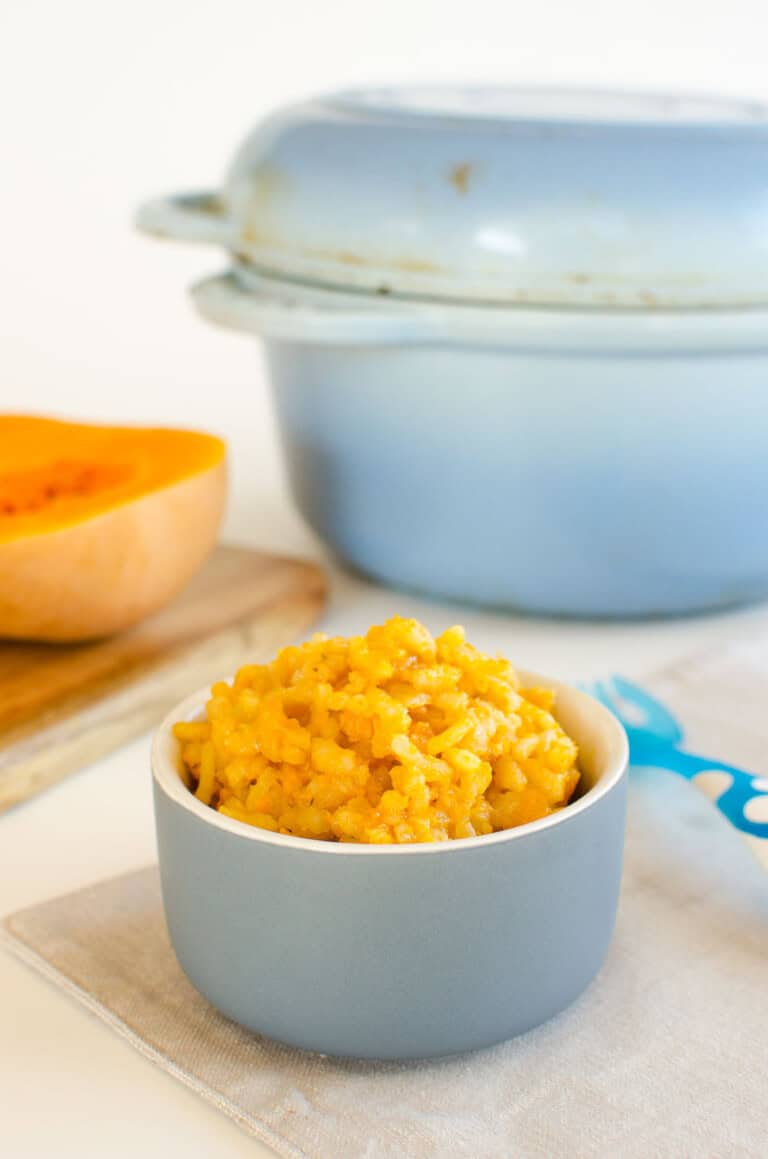 A ramekin of pumpkin risotto infant of a blue ceramic Dutch oven.