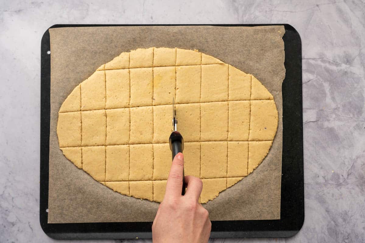 Cracker dough being cut into rectangles using a pizza roller. 