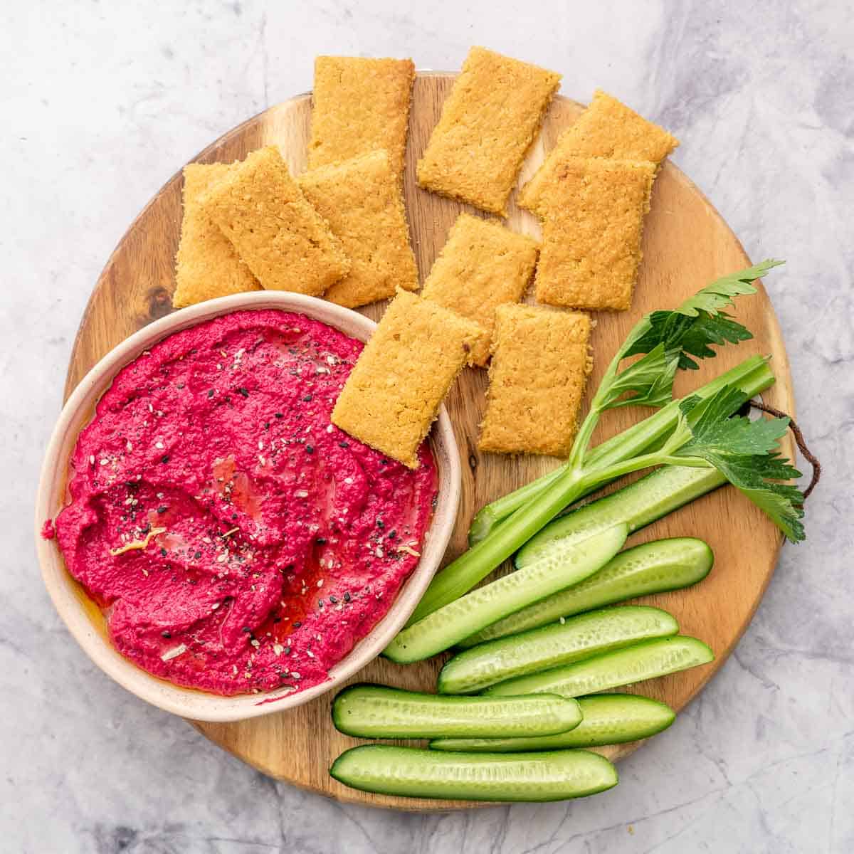Crackers, beetroot hummus and vegetable sticks on a wooden platter. 