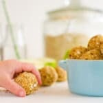 A chads hand holding an oatmeal ball next to a small blue dish filled with more oat balls.