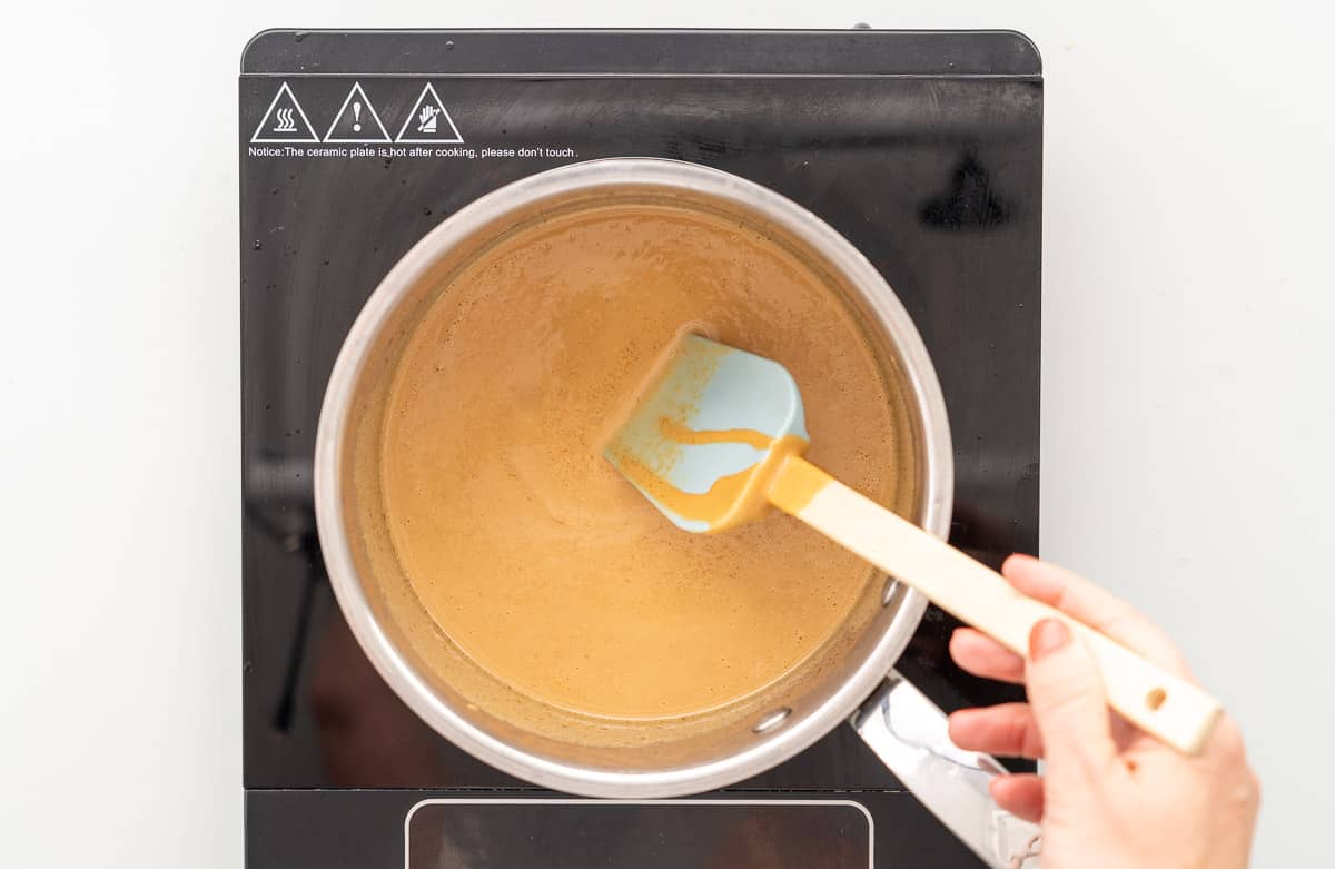 Smooth peanut butter caramel being stirred with a spatula in a saucepan.
