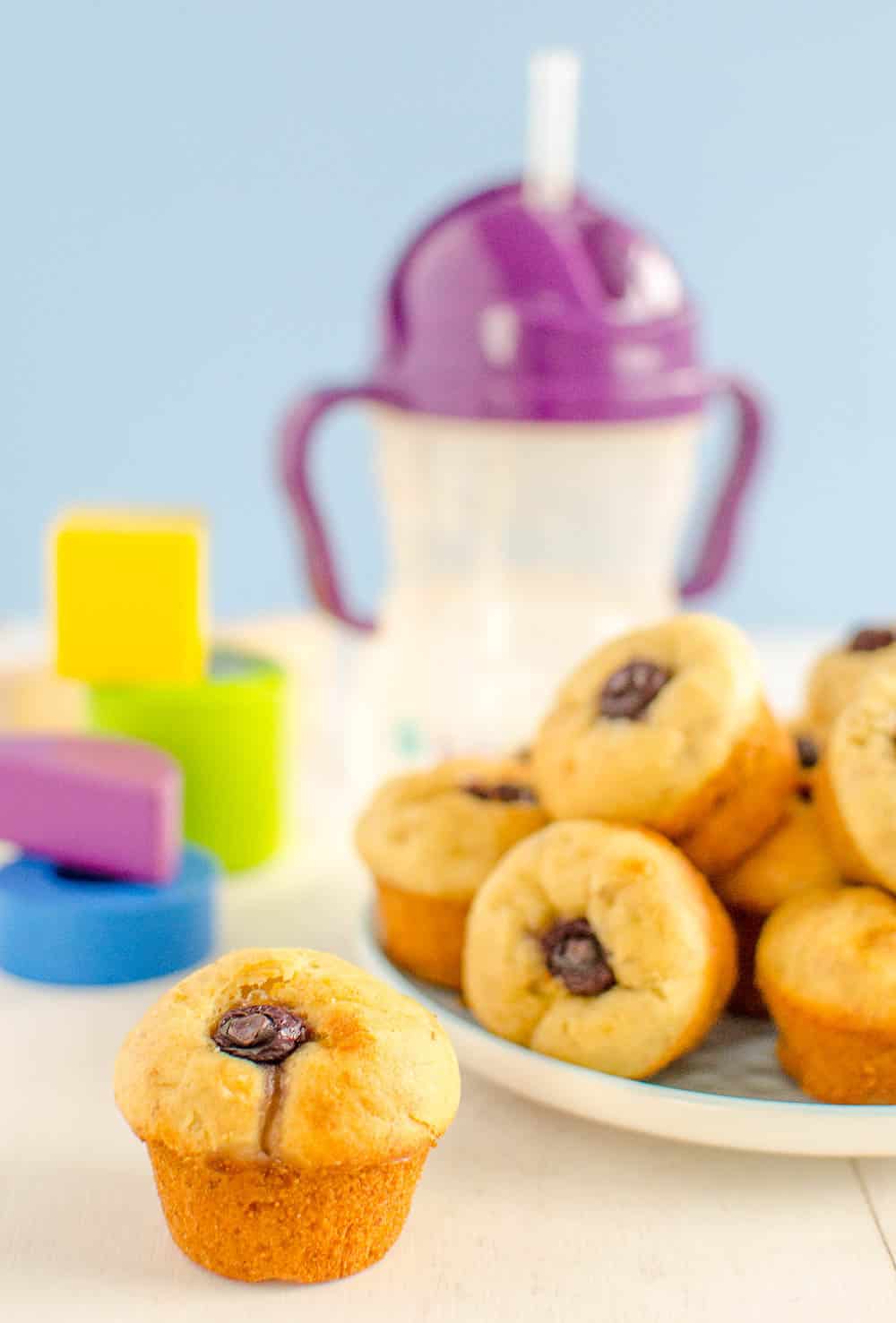 A plate full of banana blueberry muffins with colourful building blocks and a childs cup