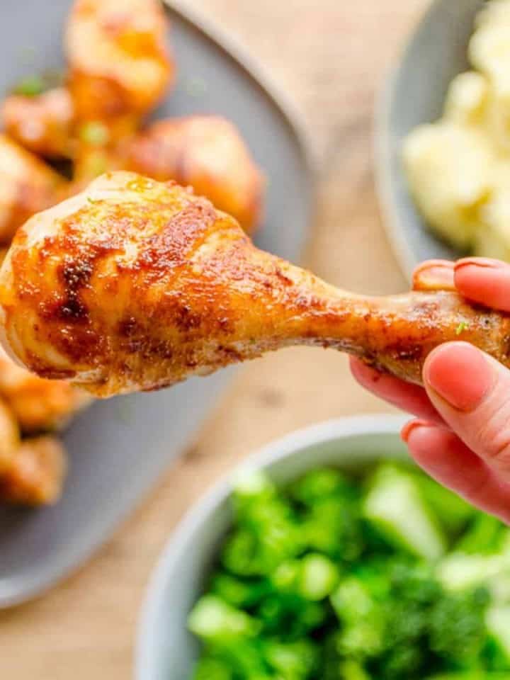 Woman's hand holding a chicken drumstick above a family dinner table.