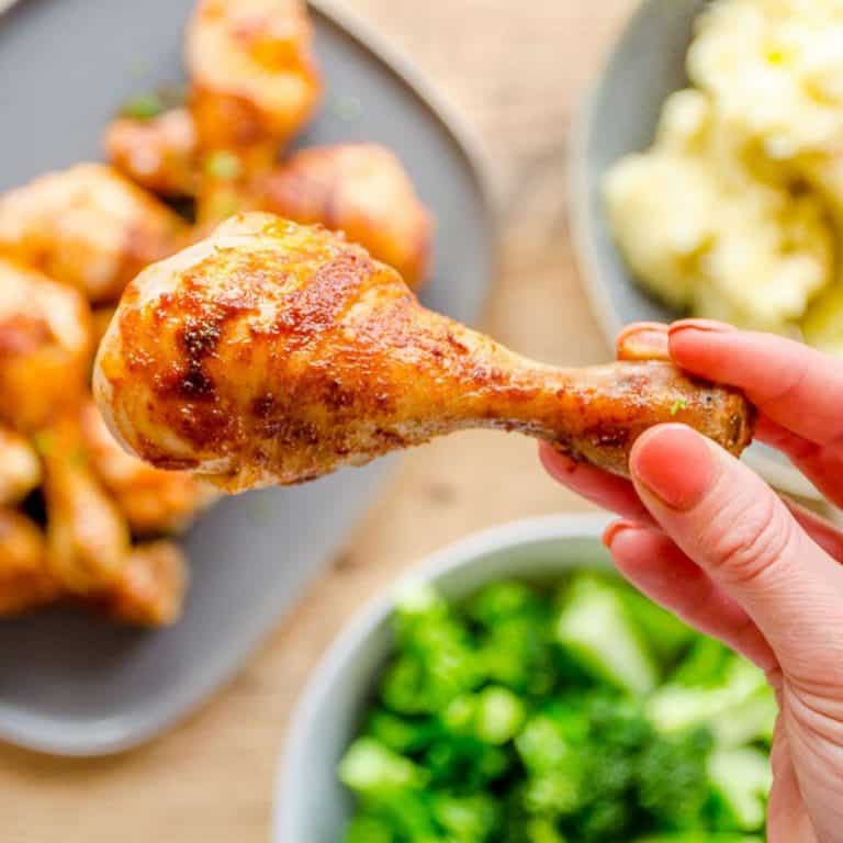 Woman's hand holding a chicken drumstick above a family dinner table.