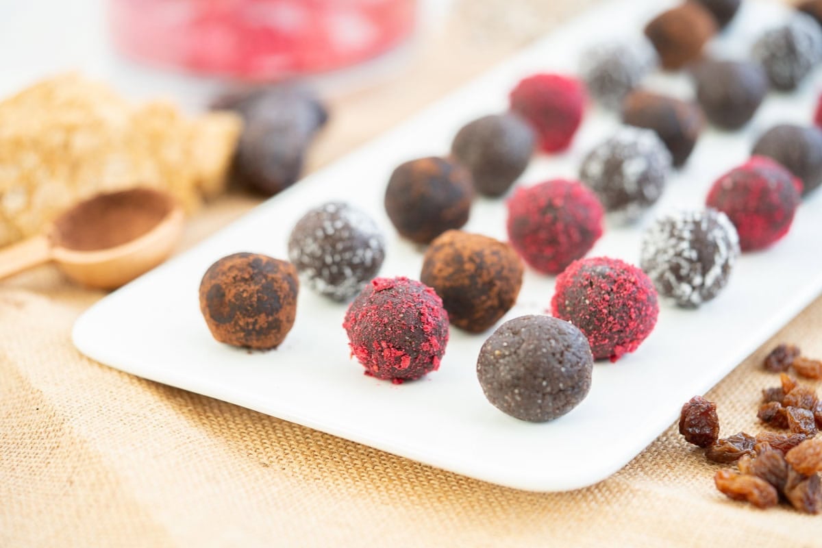 Chocolate bliss balls rolled in coconut, berry powder and cocoa on a white platter. 