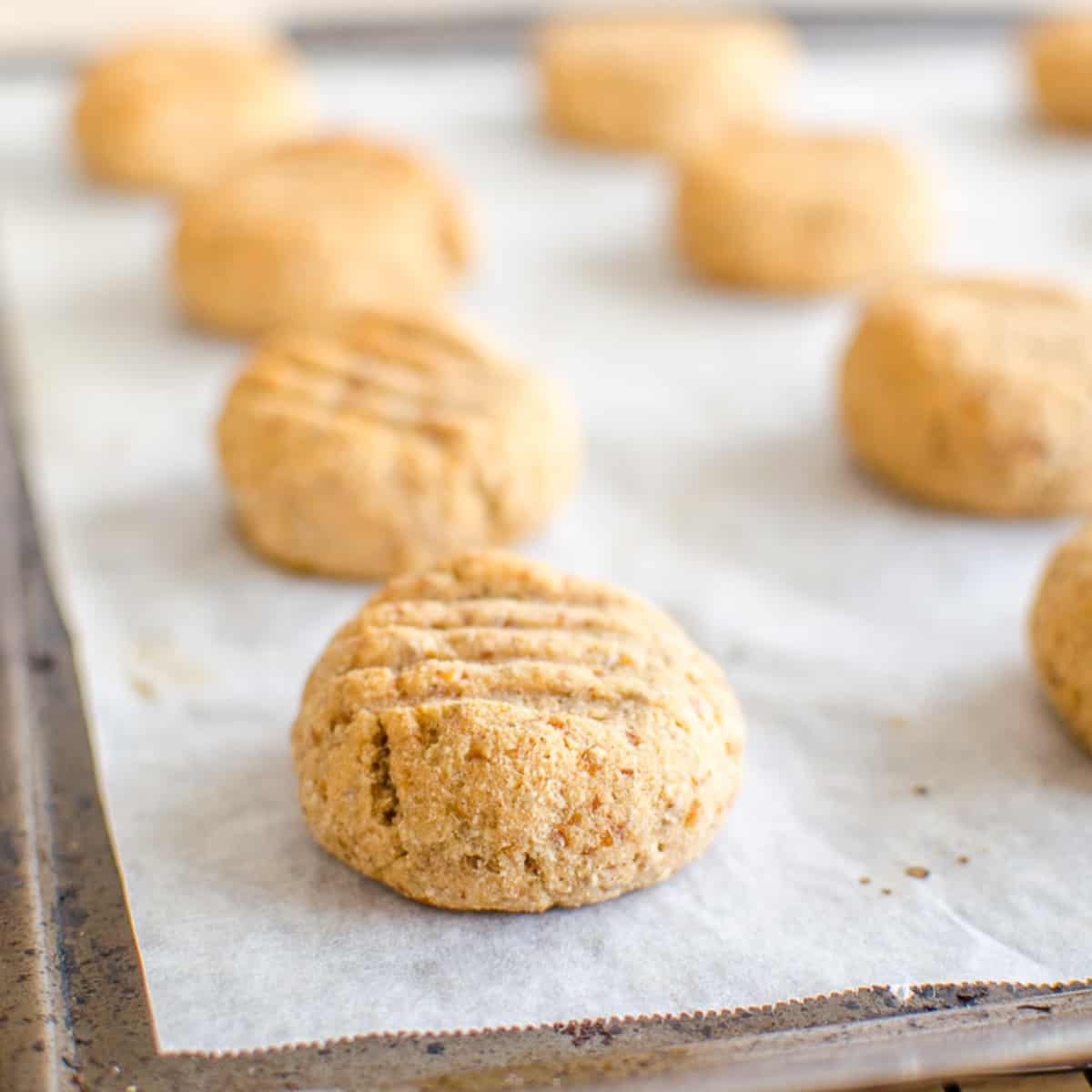 Small golden cookies with fork marks on a lined baking sheet. 