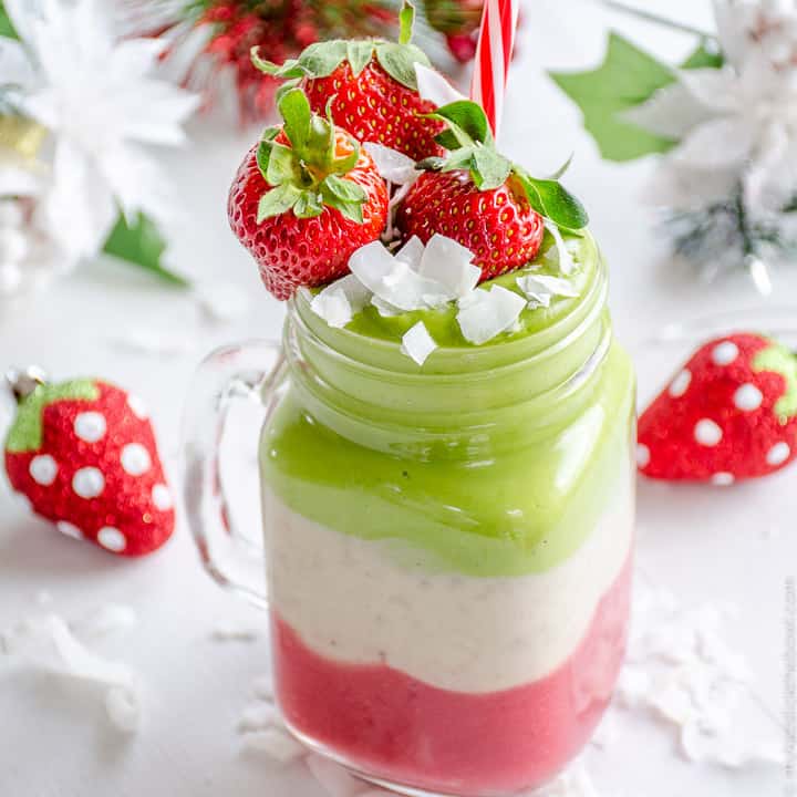 A green red and white layered smoothie in a glass jar surrounded by Christmas decorations