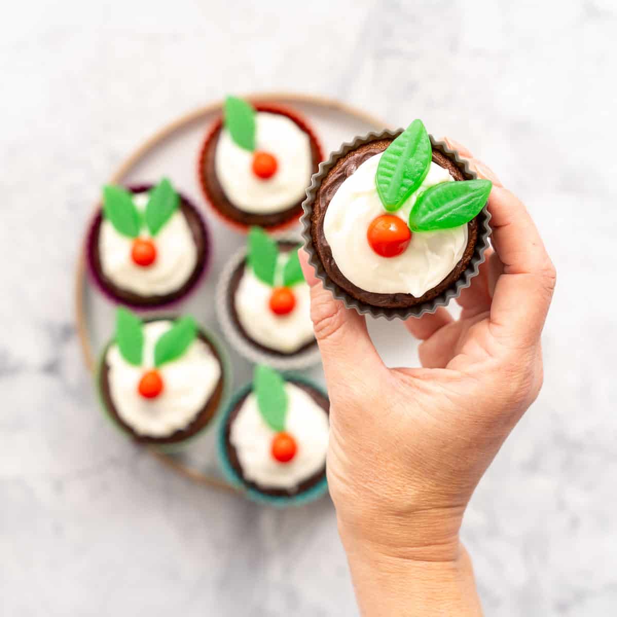 A cupcake decorated to look like a figgy pudding with frosting and candy being held up to the camera.