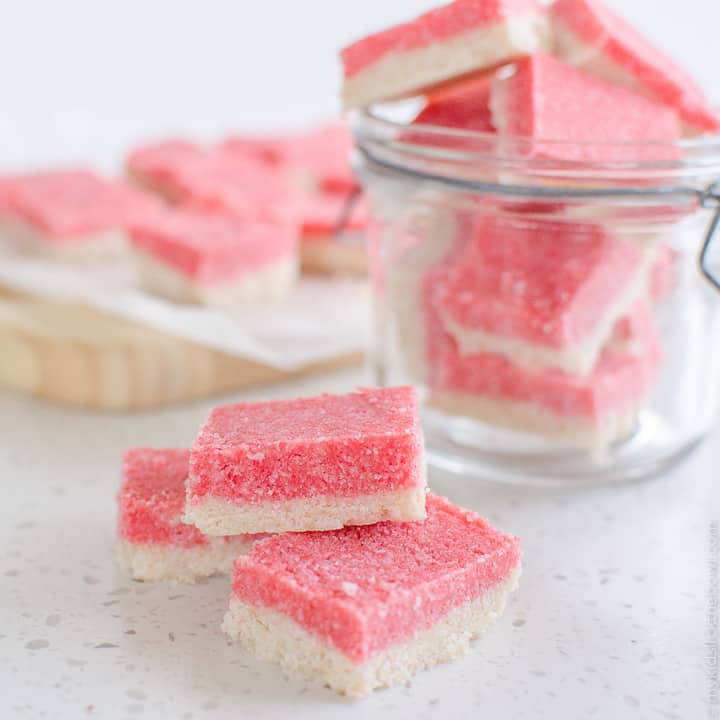 3 slices of coconut ice in foreground with a jar of coconut ice in the background