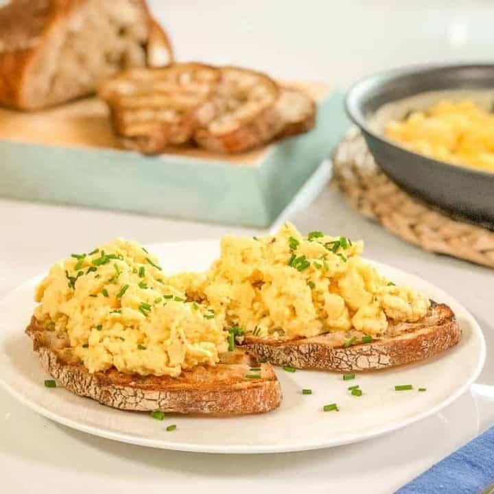 Two pieces of sour dough toast topped with scrambelled eggs.
