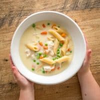 child's hands holding bowl of chicken pasta soup