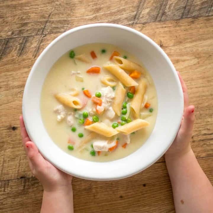 child's hands holding bowl of chicken pasta soup