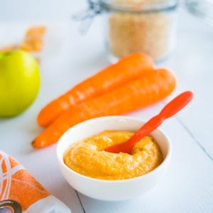 quinoa baby cereal with carrotand apple, in small white bowl with orange spoon