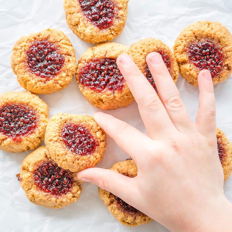 Peanut Butter and Jam Thumbprint Cookies, on a white background childs hand grabbing one
