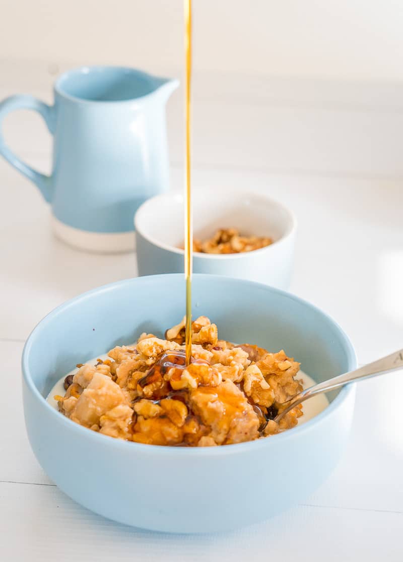 slow cooker porridge in a blue topped with walnuts, maple syrup being poured on top