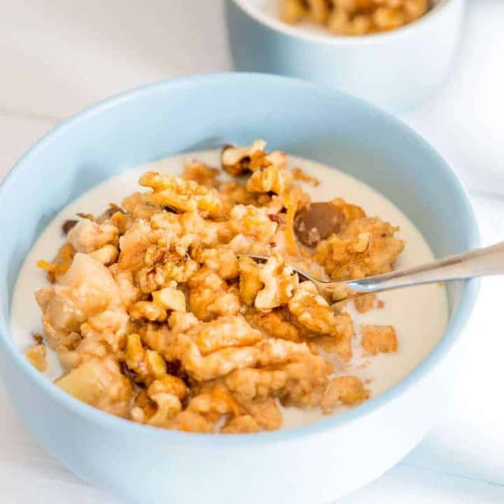 slow cooker porridge in a blue bowl topped with walnuts milk and maple syrup, chunks if soft apple visible