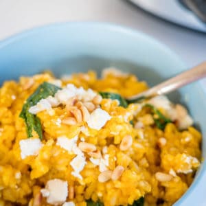 Slow Cooker Risotto, in a blue bowl topped with feta and pinenuts