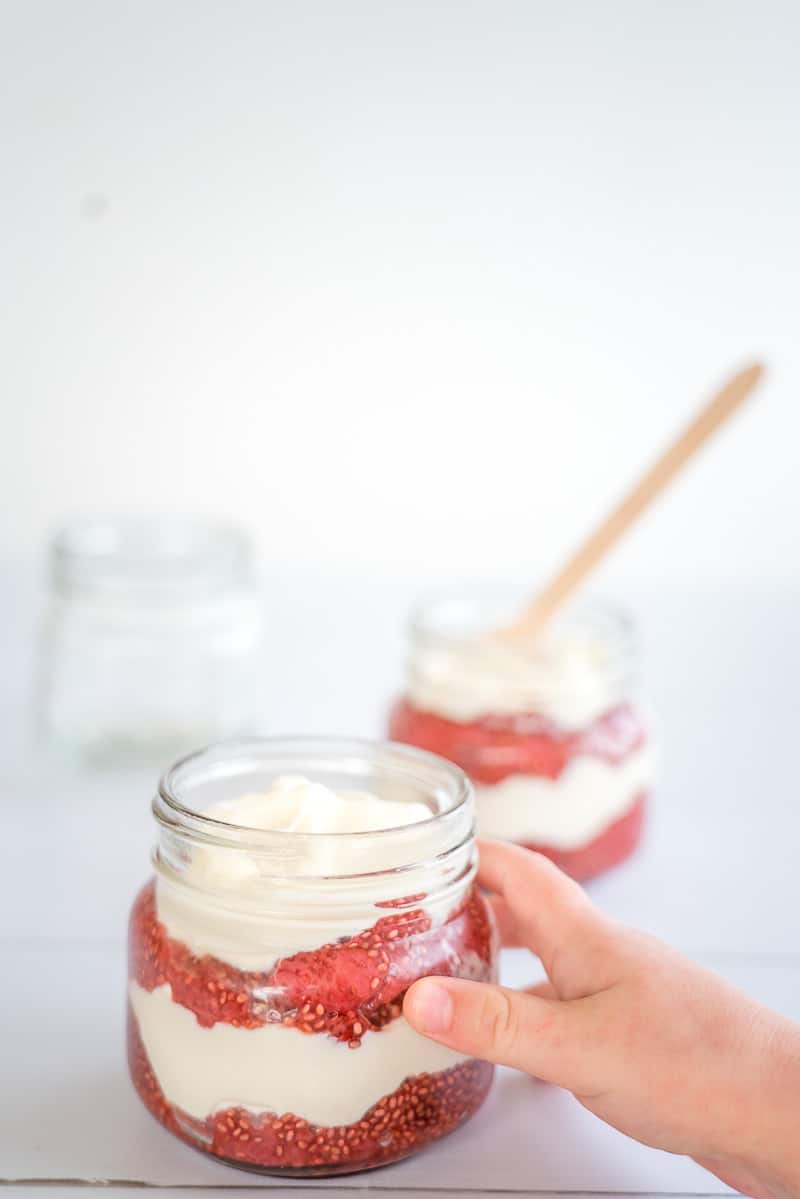 Strawberry chia yoghurt parfaits a childs hand reaching to grab a small layered parfait