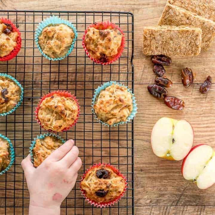 apple and date muffins on a cooling rack, child's hand reaching out to grab one