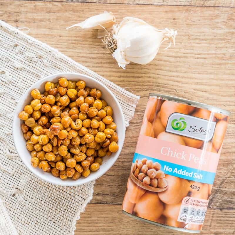 Crunchy roasted chickpea in a white bowl, with a whole clove of garlic and a tin of chickpeas