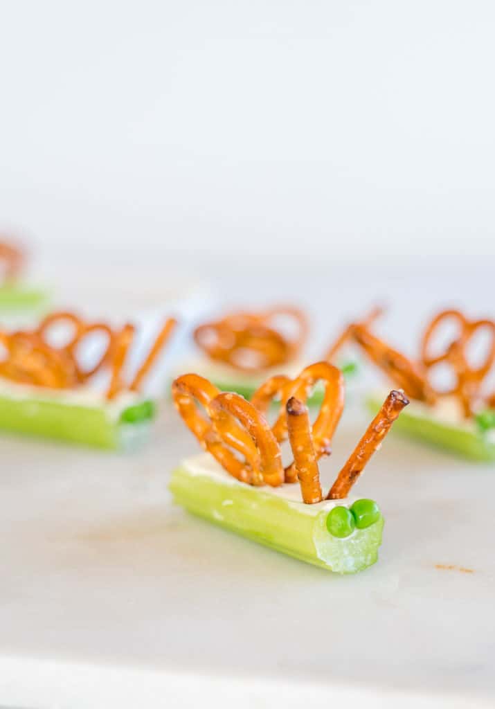 celery sticks filled with cream cheese, topped with pretzles to create butterfly wings and peas for eyes.