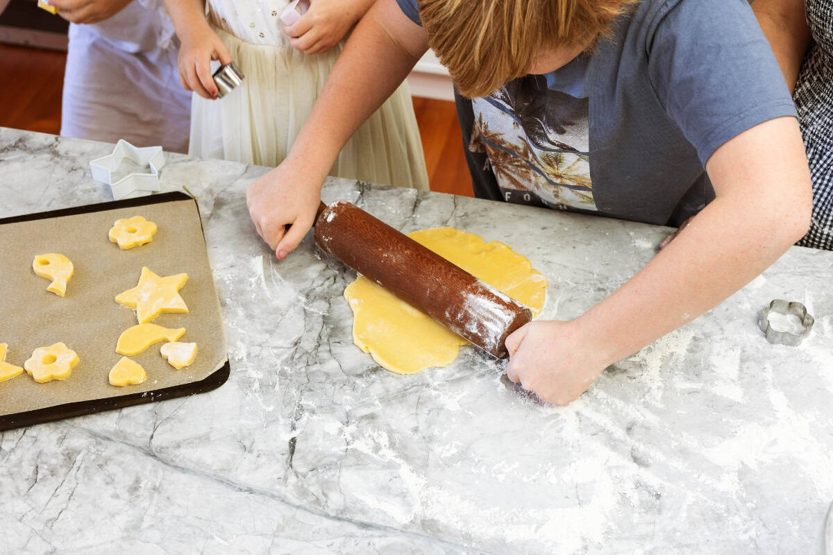 A boy rolling dough on a marble bench top with a wooden rolling pin. 