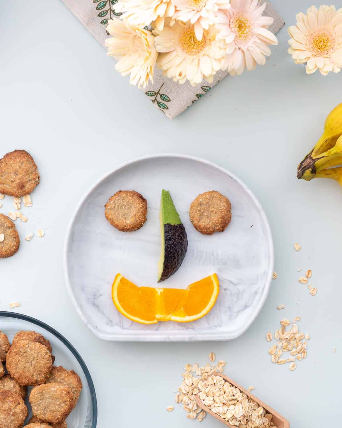 A silicone baby plate with food placed on it to look like a face. cookie eye, avocado nose, orange slice mouth.