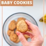 A hand holding a small cookie above a round glass container full of oatmeal cookies on a bench next to a bunch of bananas, with tex overlay for pinterest.