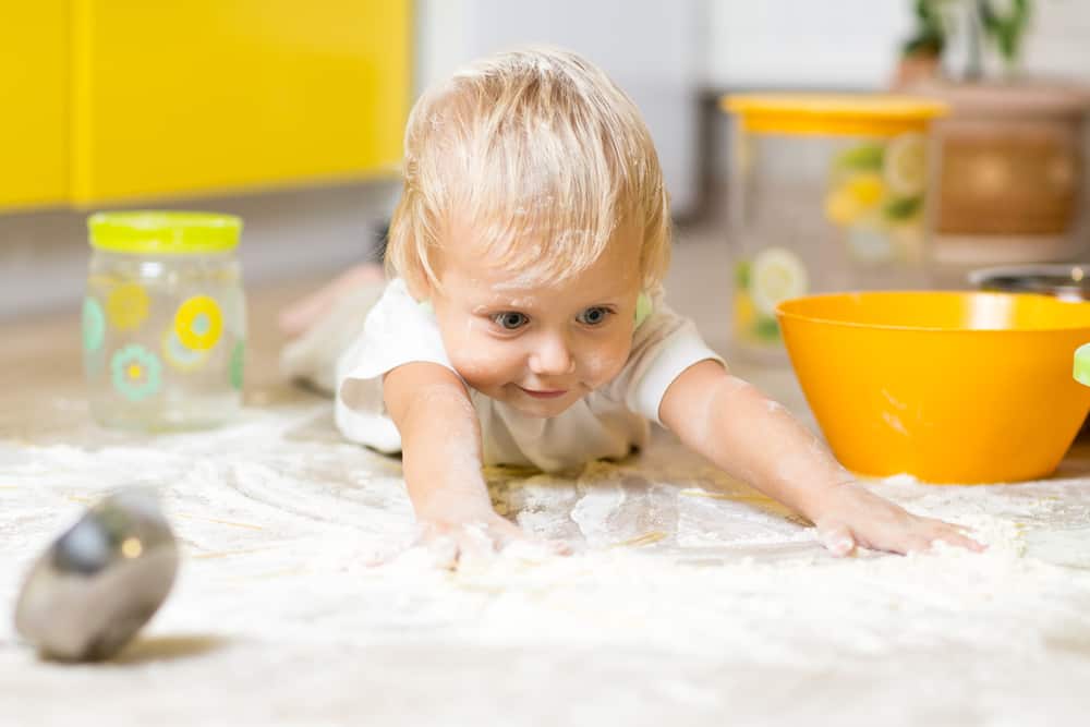 Cooking with kids is messy, Little boy child laying on very messy kitchen floor. Toddler covered in white baking flour.