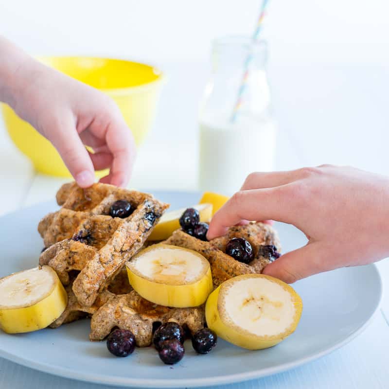 Healthy waffles on a plate with kids hands reaching for them