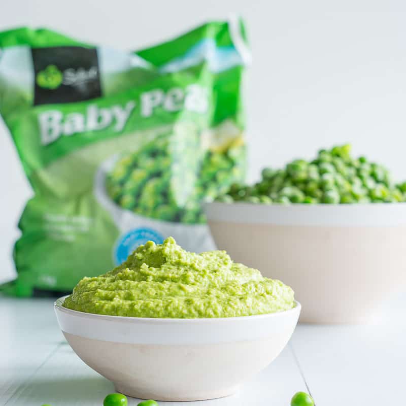 Pea pesto in a small bowl with frozen peas in the background