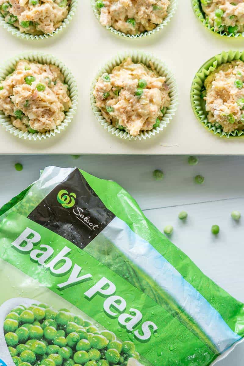 Savoury muffin batter uncooked in a cream muffin tin with a bag of frozen peas