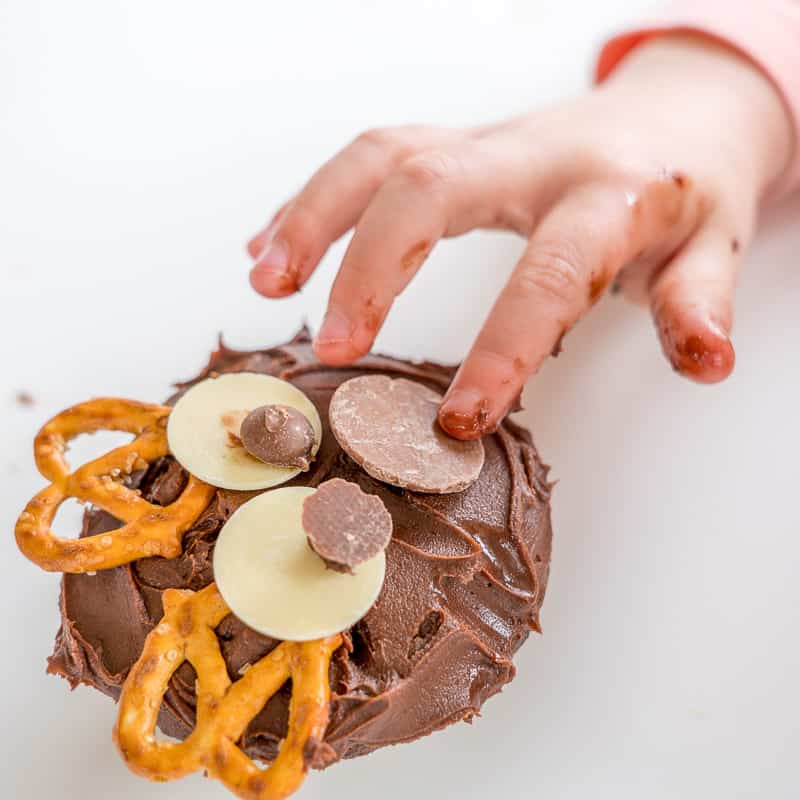 A cupcake being decorated like a reindeer by a childs hand. 